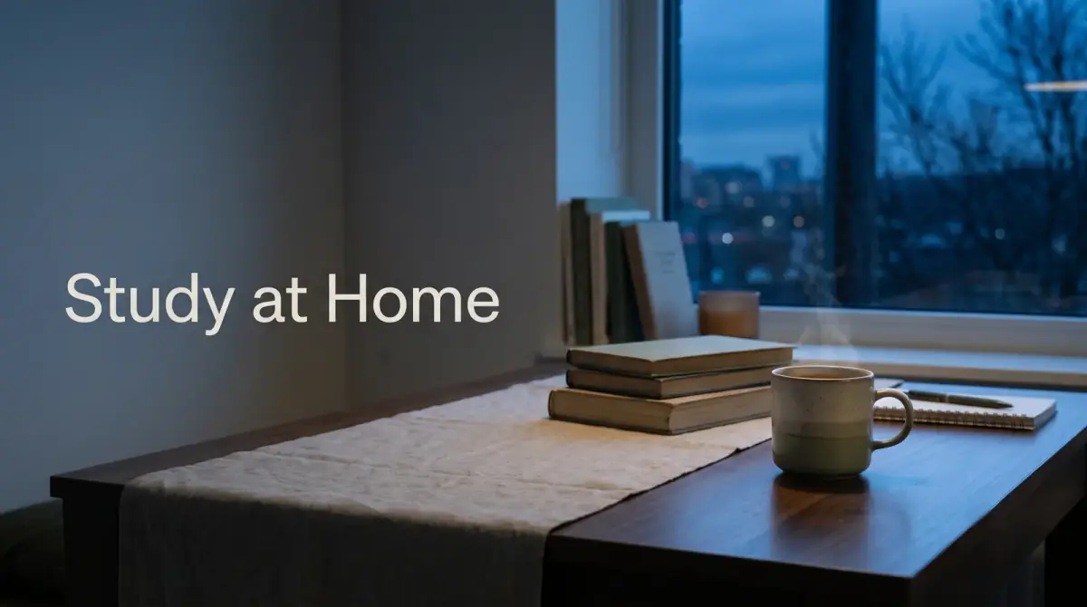 a quiet home desk by a window with books and a warm drink
